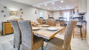 A dining area with a wooden table and woven chairs, a kitchen in the background, and a decorative wall with star-like patterns. - Steps to Sand: Resort Escape on South Padre Island (South Padre Island)