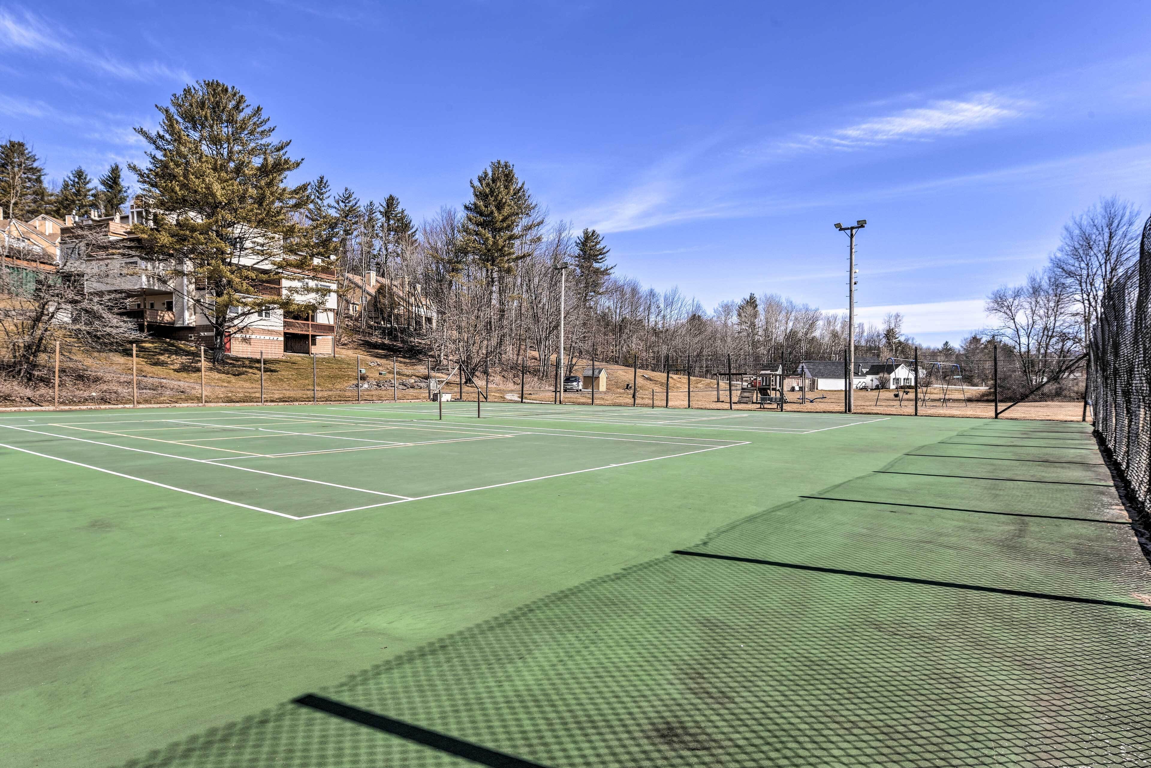 Un court de tennis en plein air, doté d’une surface verte, entouré d’arbres et d’immeubles d’habitation.