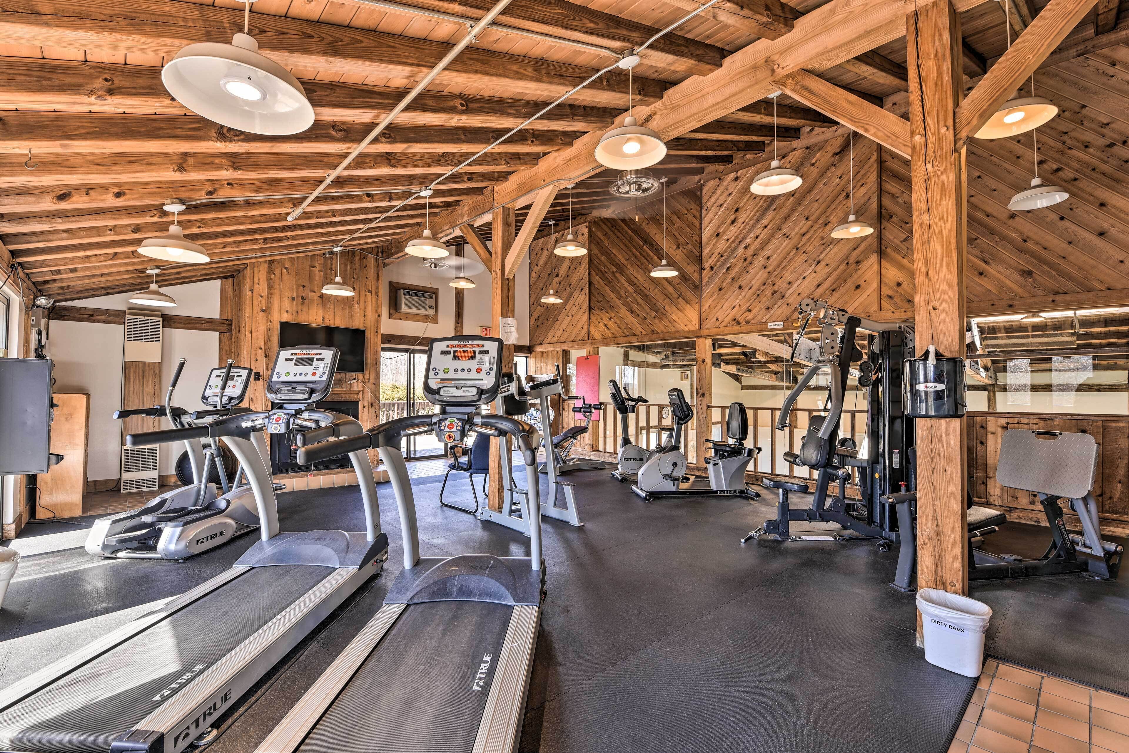 A gym with treadmills, elliptical machines, and weight equipment under a wooden ceiling with exposed beams.