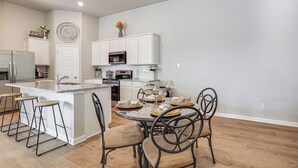 Une cuisine moderne avec des meubles blancs, un îlot central doté de tabourets de bar et un coin repas avec une table ronde et des chaises.