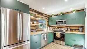 A modern kitchen with stainless steel appliances, teal cabinets, and a wooden backsplash. - Game Room & Resort Perks! Split Rock Retreat (Lake Harmony)