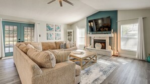 A living room with a sectional sofa, a wooden coffee table, a fireplace, and a ceiling fan. - Modern Coastal Escape 1 Mi to Anclote River Park (Holiday)