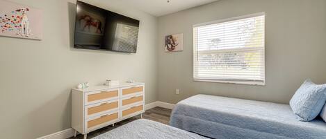 A bedroom with two beds, a ceiling fan, a dresser, and artwork on the walls.