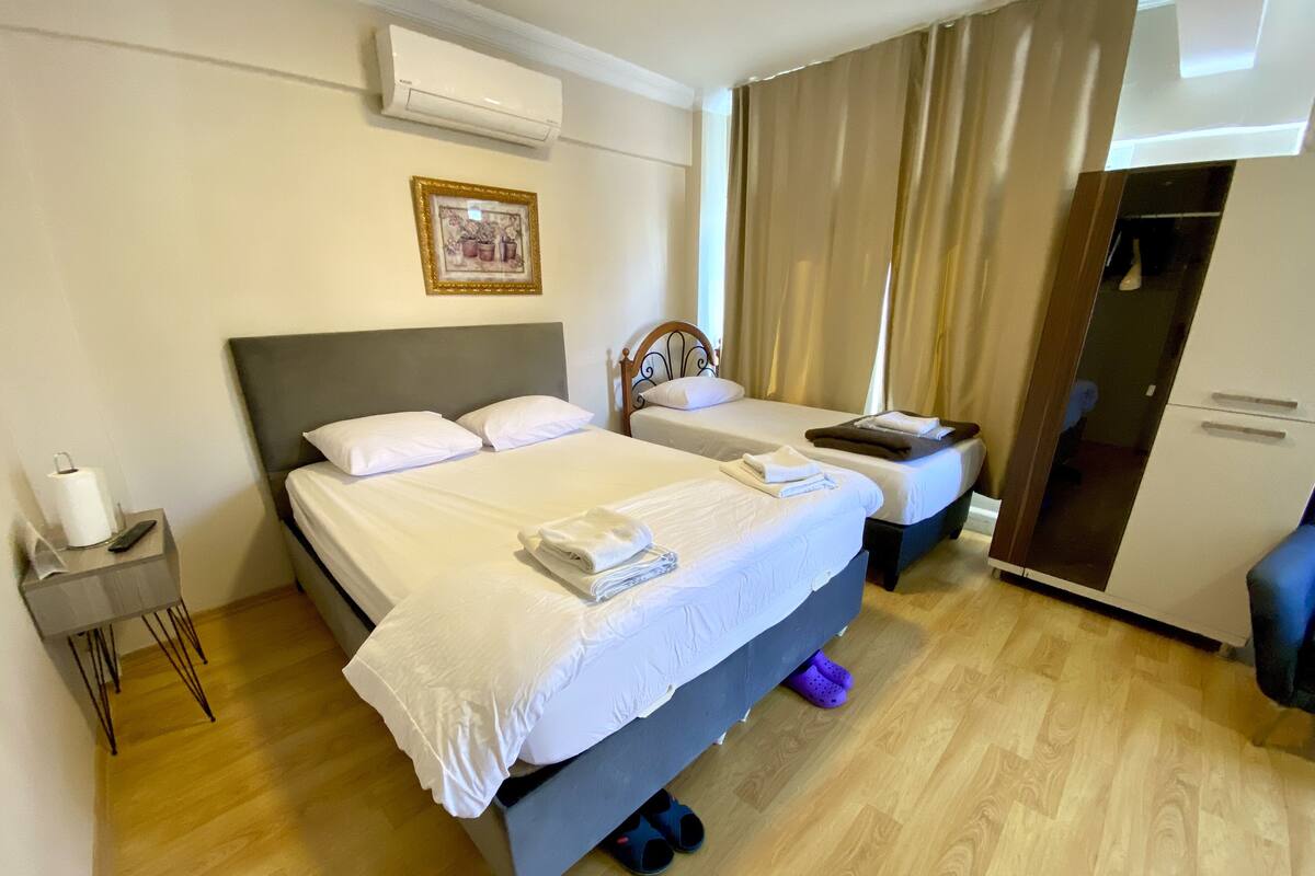A hotel room with two beds, a wardrobe, a mirror, and a small bedside table with a remote control.