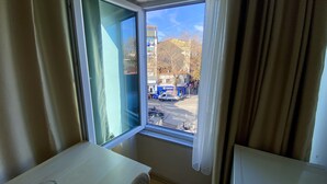 A room with a large window, a white table, and a clear view of the street outside. - Meydan Pansiyon (İstanbul)