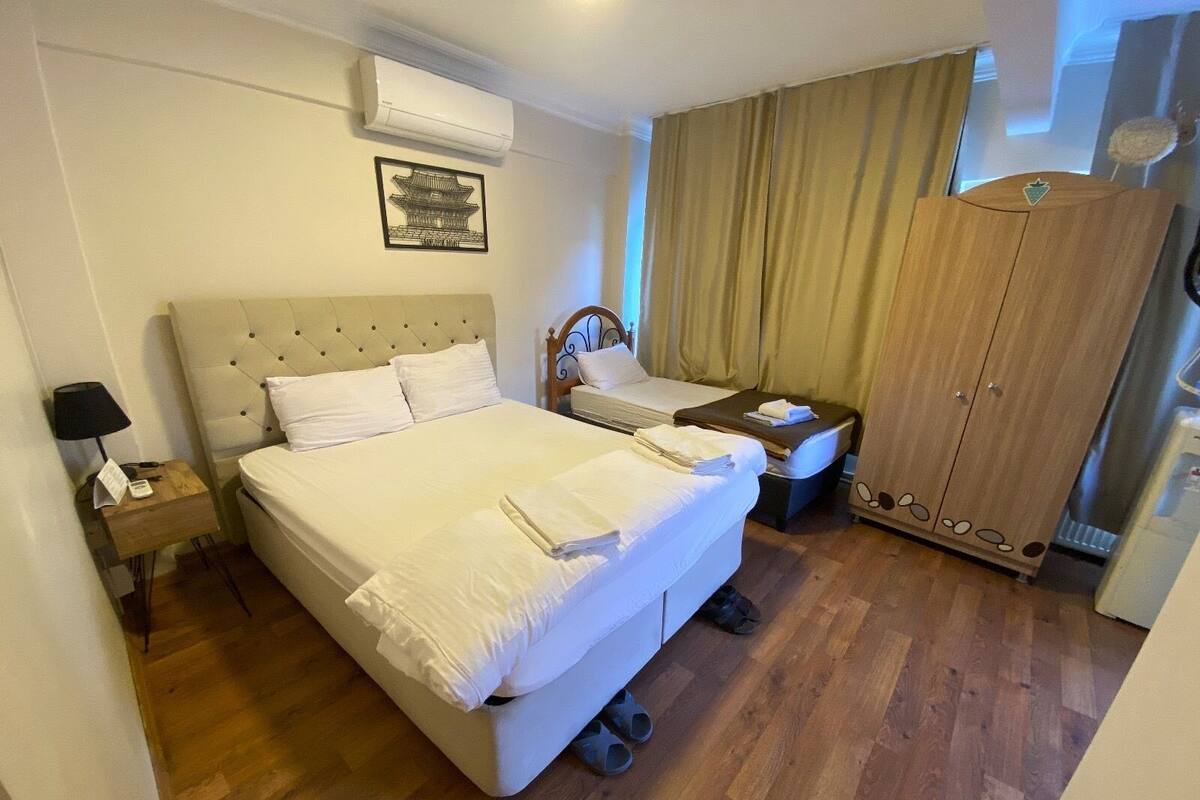 A hotel room with a large bed, a smaller bed, a wardrobe, a nightstand, and a wall-mounted air conditioner.