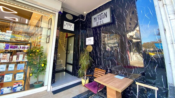 A hotel entrance with a marble facade, a wooden bench, and a small table. - Meydan Pansiyon (İstanbul)