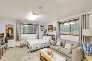 Un dormitorio bien iluminado con cama, sofá, mesa y silla. Hay ventanas con cortinas, un espejo y una lámpara de pared.