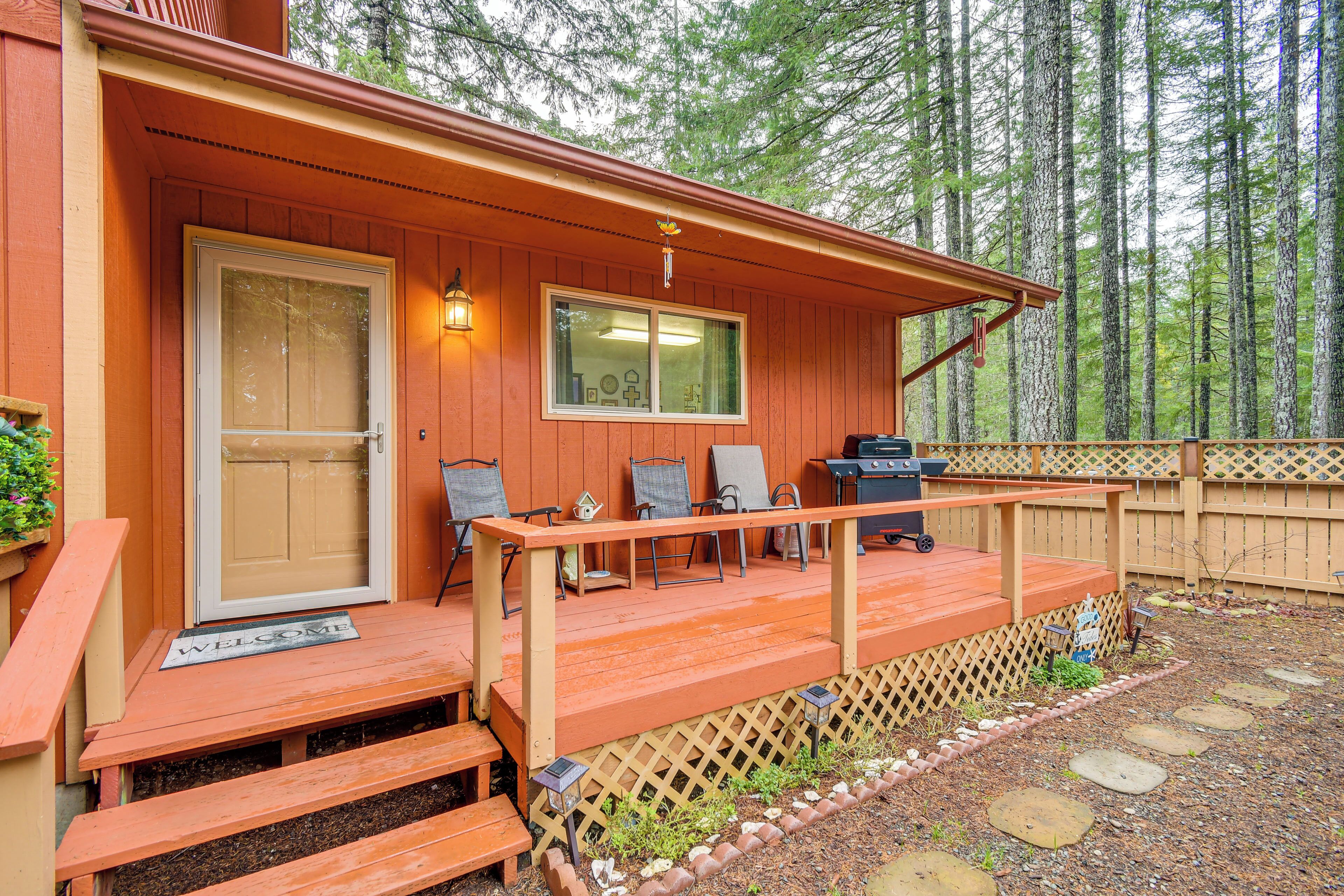 A wooden cabin with a porch, a welcome mat, and a grill.