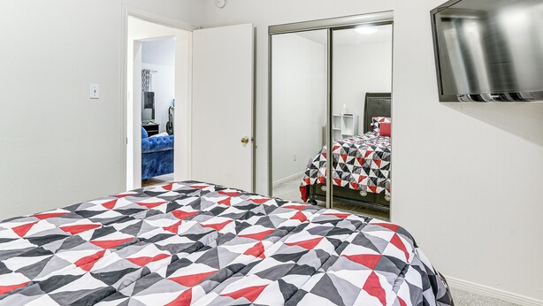 A bedroom with a bed covered in a geometric patterned bedspread, a wardrobe, and a mirror on the wall. - Extended Stay in Sugar Land! Family Home w/ Yard (Sugar Land)