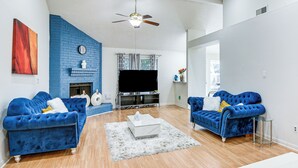 A living room with two blue sofas, a white coffee table, a fireplace, and a flat-screen TV. - Extended Stay in Sugar Land! Family Home w/ Yard (Sugar Land)