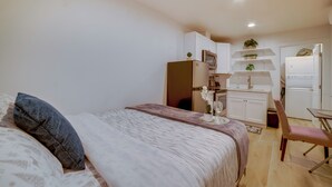 A bedroom with a bed, a chair, a small table, and a kitchenette in the background. - Nurse-ready Rental 10 Mi to Dtwn Riverside! (Moreno Valley)