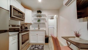 A compact kitchen with white cabinets, a built-in microwave, and a small dining area with a table and chair. - Nurse-ready Rental 10 Mi to Dtwn Riverside! (Moreno Valley)