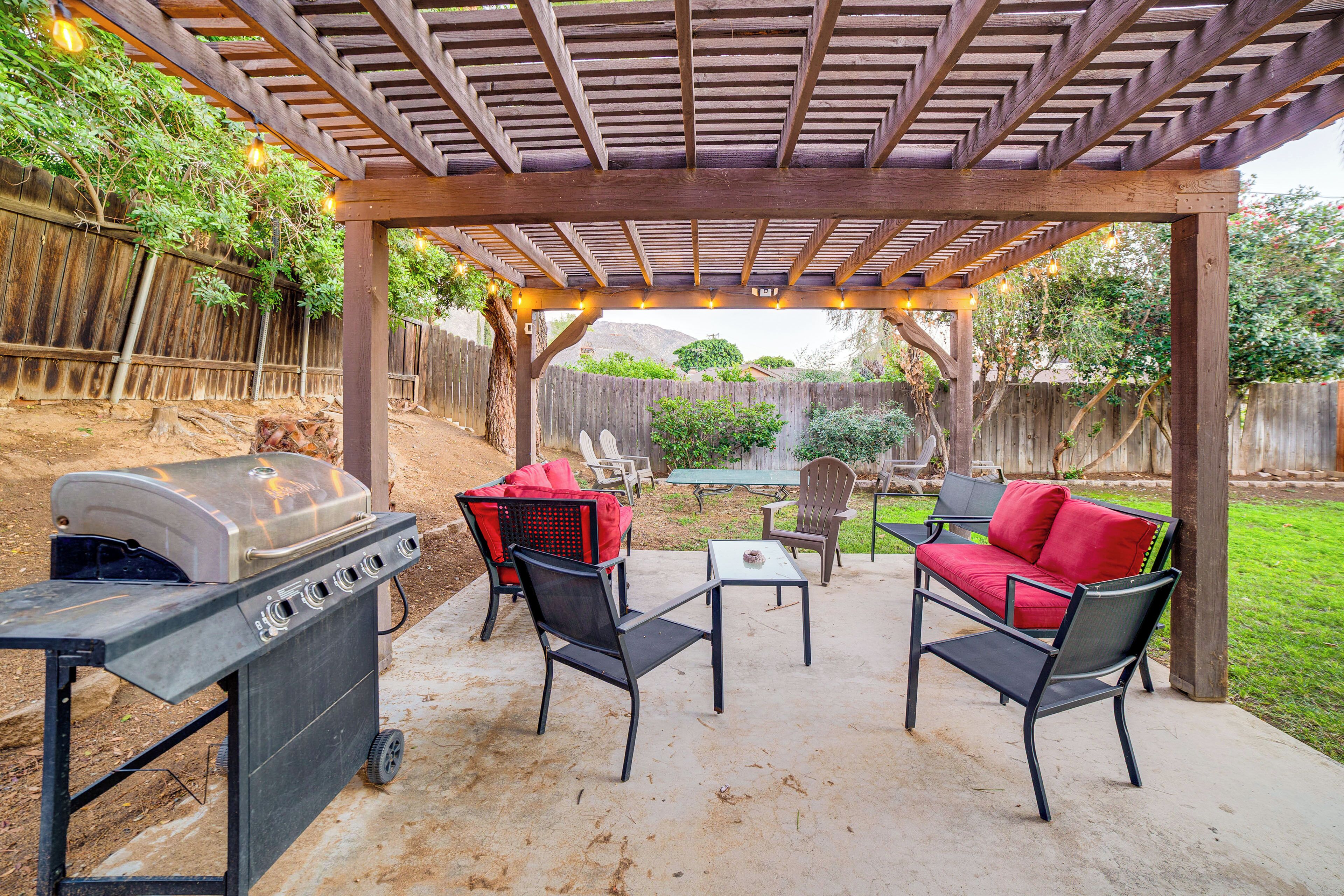 An outdoor patio with a wooden pergola, a grill, and seating area with chairs and a table.
