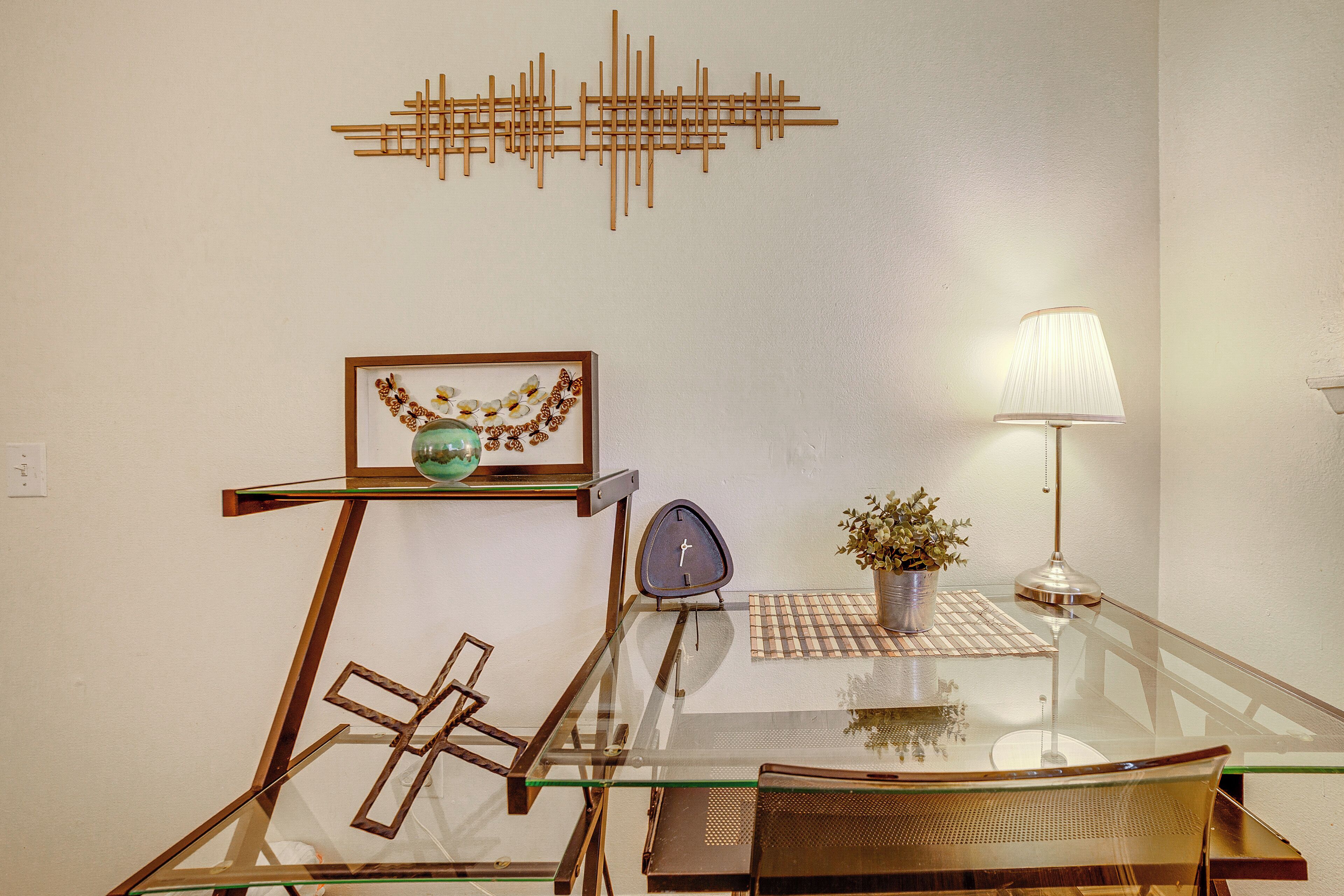 A modern dining area with a glass table, metal chairs, a wall-mounted clock, a decorative plant, and a wall art piece.