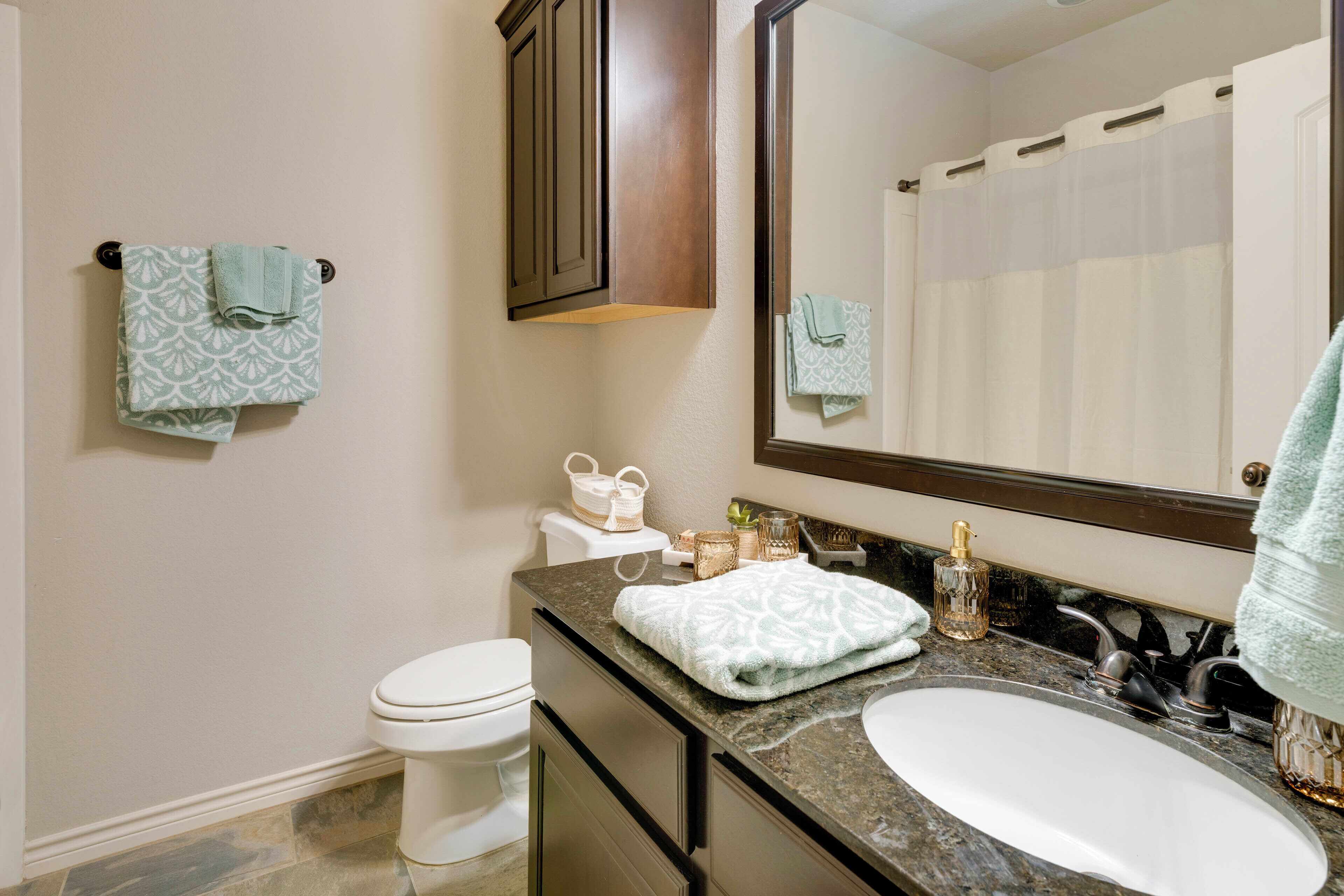 A bathroom with a white toilet, a sink with a large mirror above it, and two towels hanging on the wall.