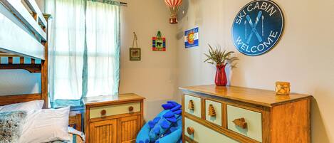 Un dormitorio con una cama individual doble, un aparador, un reloj de pared y un ventanal con cortinas.