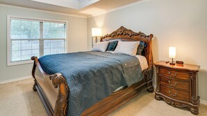A bedroom with a large bed, a nightstand with drawers, a ceiling fan, and a window with blinds. - Gateway to Aggieland! College Station Family Home (College Station)