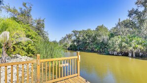 A wooden deck with a railing overlooking a calm river, surrounded by lush greenery and trees. - Canal-front Home w/ Fishing Dock in Port Charlotte (Port Charlotte)