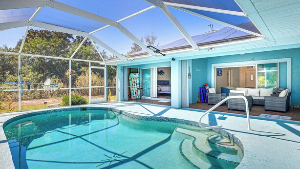 A swimming pool with a glass enclosure, a sunroom with a sofa and a chair, and a door leading to a bedroom. - Canal-front Home w/ Fishing Dock in Port Charlotte (Port Charlotte)