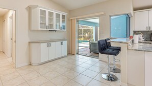 A spacious kitchen with white cabinets, a large window, and a bar area with stools. - Canal-front Home w/ Fishing Dock in Port Charlotte (Port Charlotte)