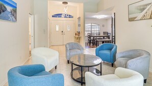 A living room with a round glass coffee table, several upholstered chairs, a white door with a decorative arch, and a dining area in the background. - Canal-front Home w/ Fishing Dock in Port Charlotte (Port Charlotte)