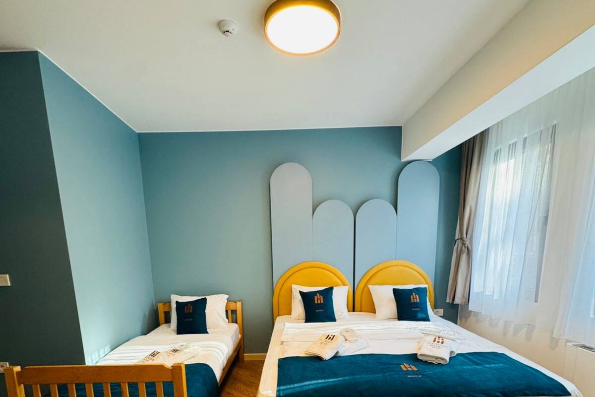 Ein Hotelzimmer mit zwei Betten, einem Holzkopfstück, einer runden Deckenleuchte und einem Fenster mit Vorhängen.