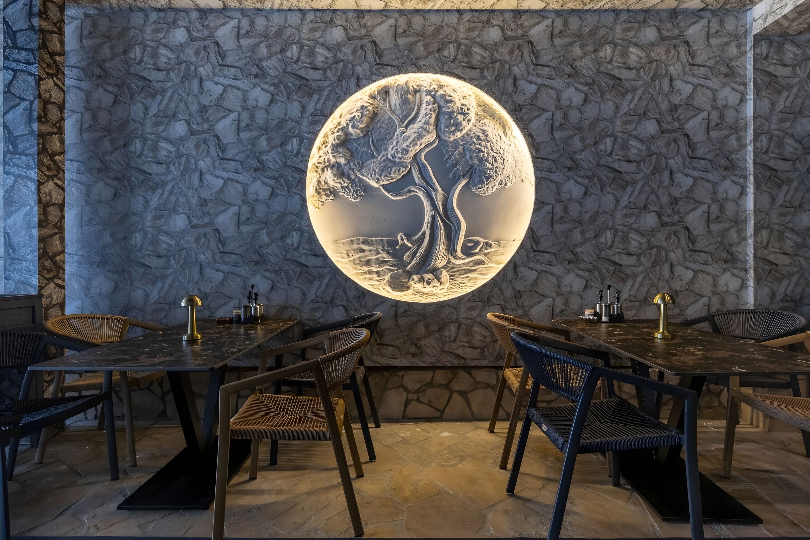Ein Restaurantinneres mit Steinsäulen, runden Tischen und Korbstühlen.