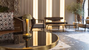 A modern living room with a round glass coffee table, a sofa with patterned cushions, and a large window with vertical blinds. - Old Stone Hotel Skopje (Skopje)