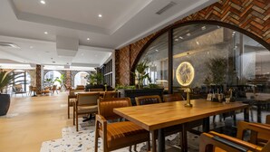 A modern restaurant interior with wooden tables and chairs, a herringbone-patterned wall, and large windows. - Old Stone Hotel Skopje (Skopje)