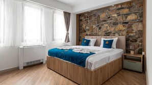 A modern bedroom with a stone accent wall, a wooden bed frame, and a nightstand with a lamp. - Old Stone Hotel Skopje (Skopje)
