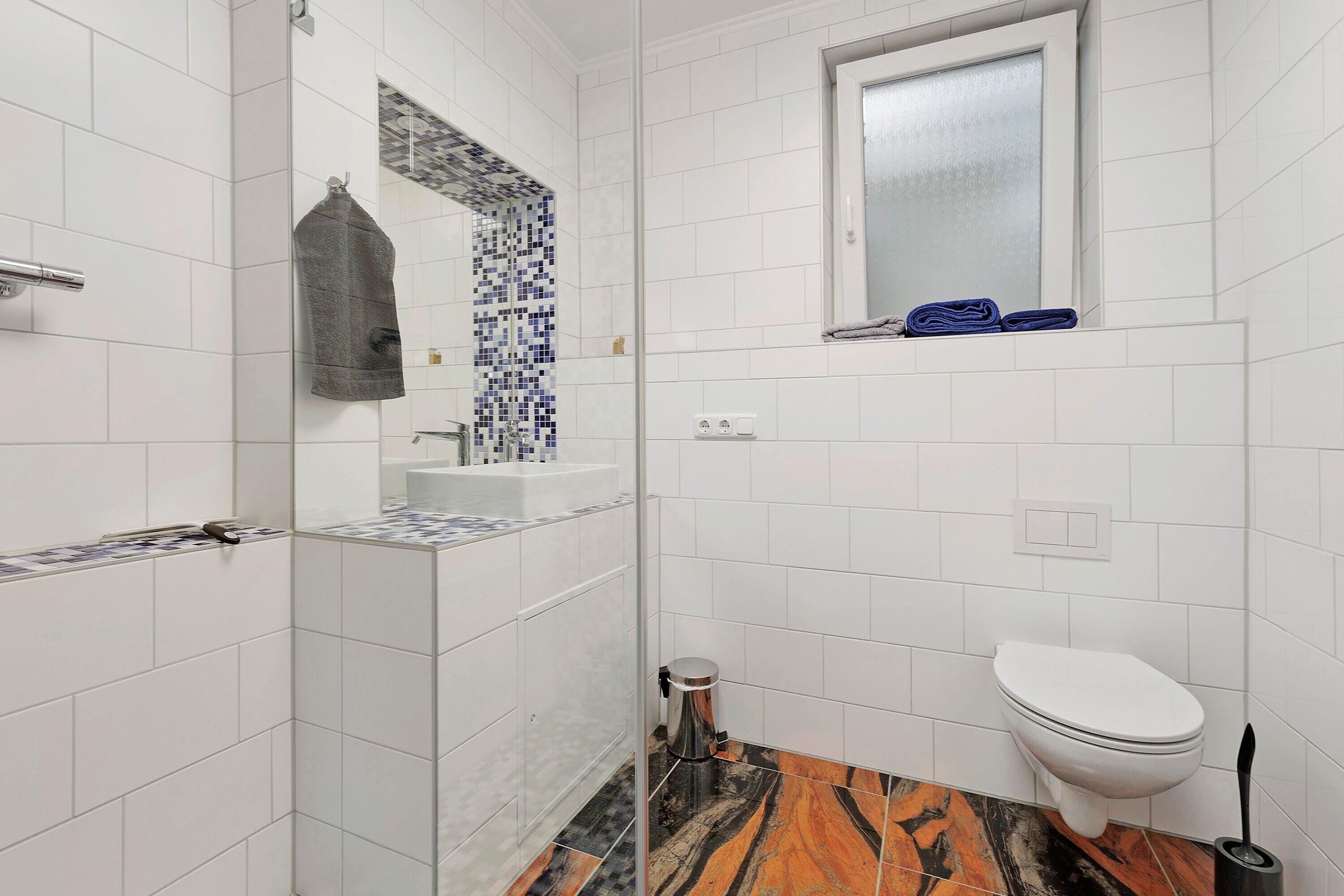 Une salle de bain avec des carreaux blancs, une douche, des toilettes, un lavabo et un miroir.