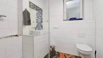 Une salle de bain avec des carreaux blancs, une douche, des toilettes, un lavabo et un miroir.