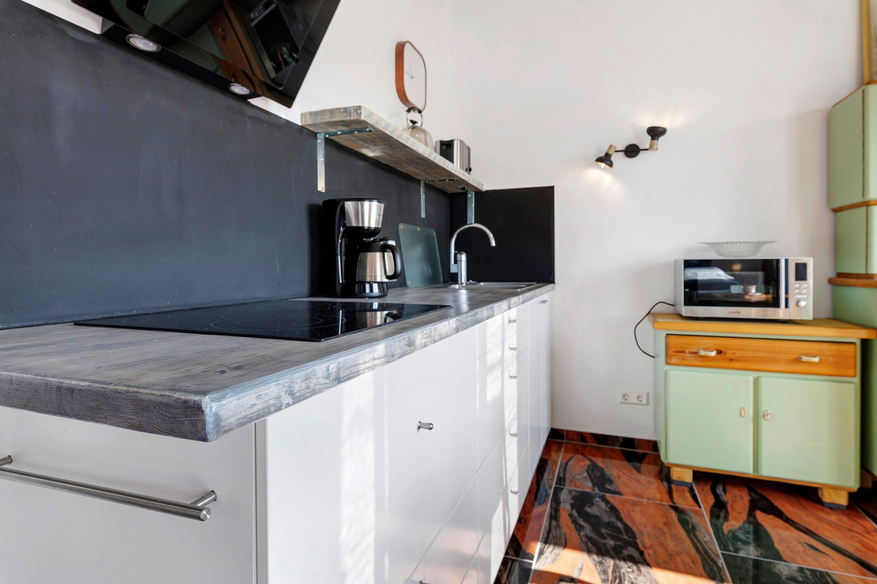A compact kitchen with a built-in stove, a coffee maker, a microwave, and a small cabinet.
