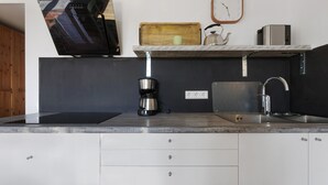 Une cuisine moderne avec un poêle noir, une machine à café, un évier et une étagère en bois sur laquelle est posée une horloge.