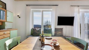 Un espace repas comprenant une table en bois, des chaises, un téléviseur et une vue sur l’extérieur.