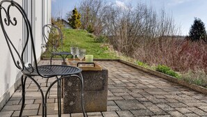 Une terrasse avec une chaise en métal, une table en bois et un bac à fleurs en pierre.