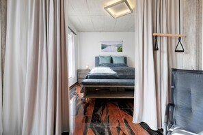Un dormitorio con cama, cortinas, cabecero, mesita de noche y lámpara de pared.