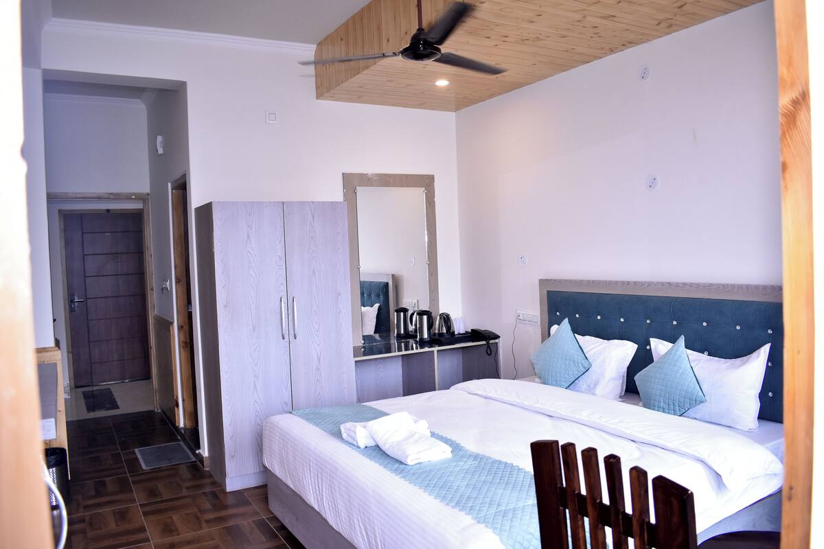 A bedroom with a bed, a wardrobe, a mirror, a ceiling fan, and a door leading to a bathroom.