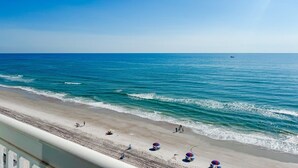 A beach with a clear sky, calm sea, and a few people and umbrellas on the shore. - The Atlantic | Direct Oceanfront | 10th Floor (Daytona Beach)