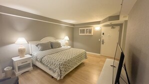 Een slaapkamer met een bed, nachtkastjes, een lamp, een deur en een raam.