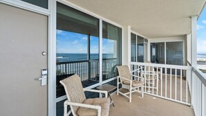 En balkon med to fletstole og et lille bord, med udsigt over et smukt havlandskab.