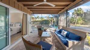 A covered patio with wicker furniture, a glass door leading to a bedroom, and a view of a pool and palm trees. - Tahitian Waters: Pet-Friendly Pool Home Just Steps to the Beach! (Sanibel)