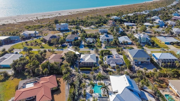 An aerial view of a coastal residential area with houses, a beach, and a clear sky. - Tahitian Waters: Pet-Friendly Pool Home Just Steps to the Beach! (Sanibel)