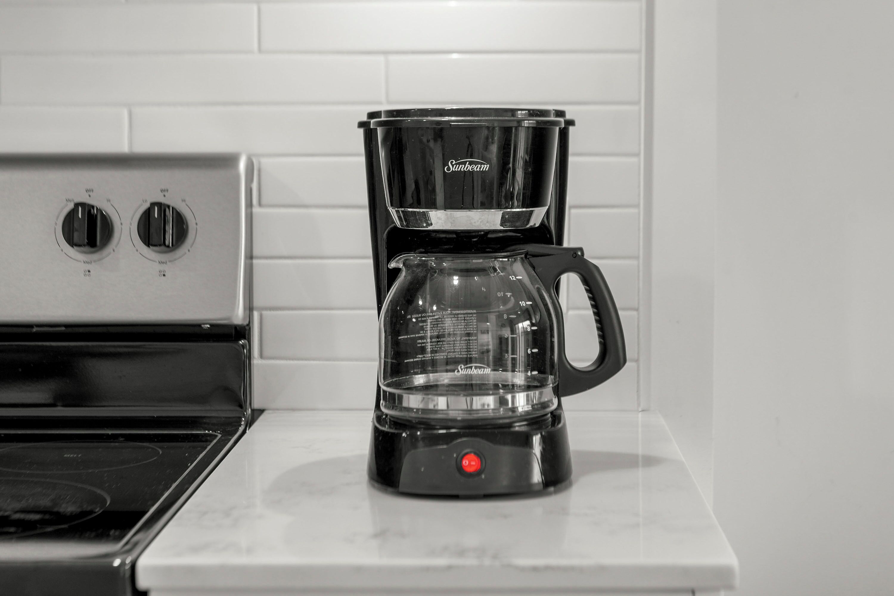 A black Sunbeam coffee maker on a white countertop next to a stove.