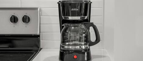 A black Sunbeam coffee maker on a white countertop next to a stove.