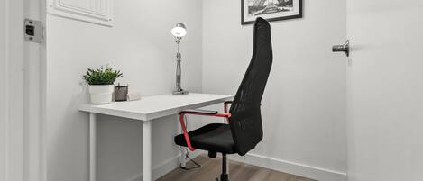 A modern office space with a white desk, a black office chair with red accents, a floor lamp, a potted plant, and a framed picture of the Eiffel Tower on the wall.