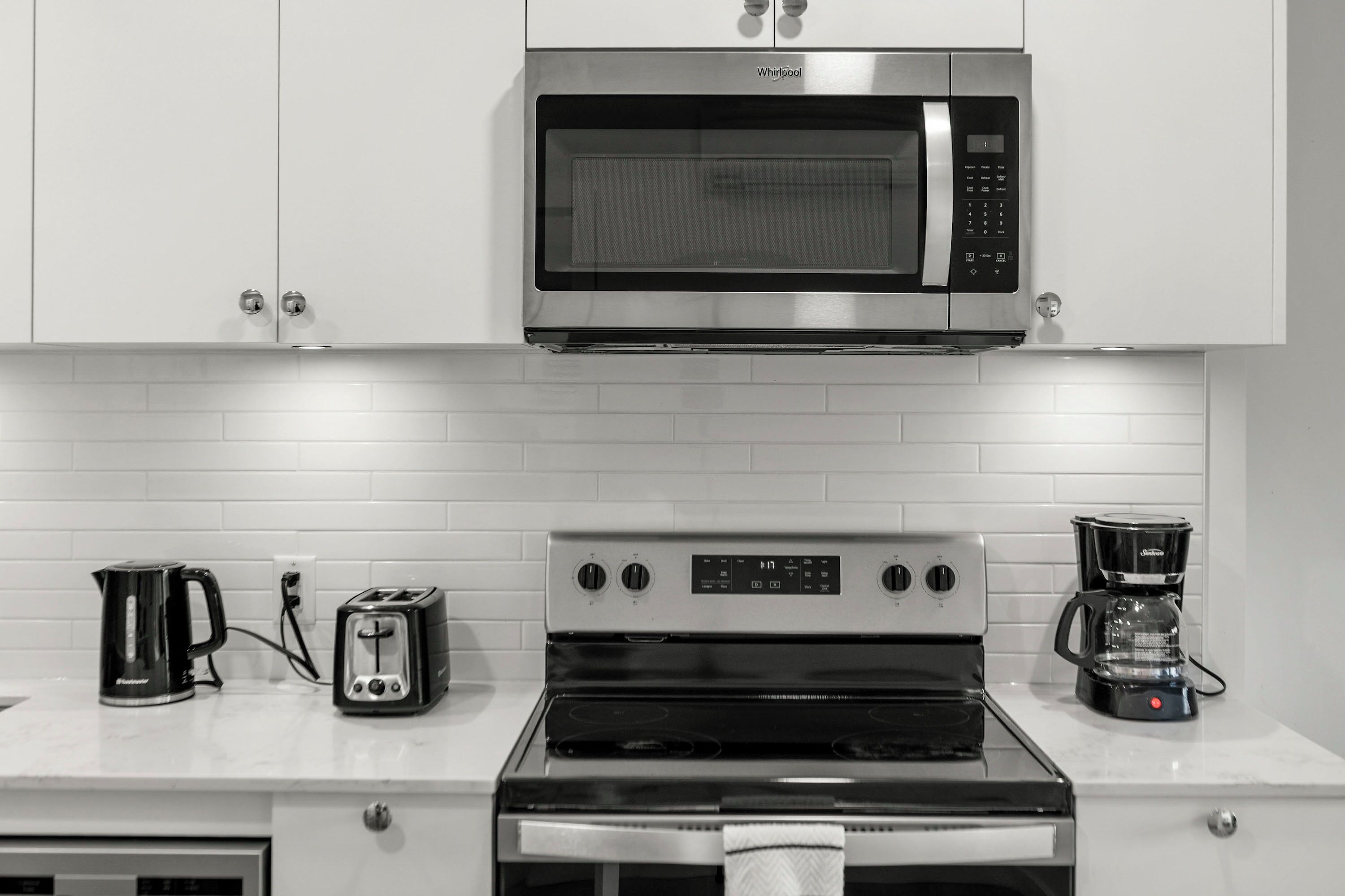 A kitchen with white cabinets, a stainless steel microwave, a toaster, a coffee maker, and a stove.