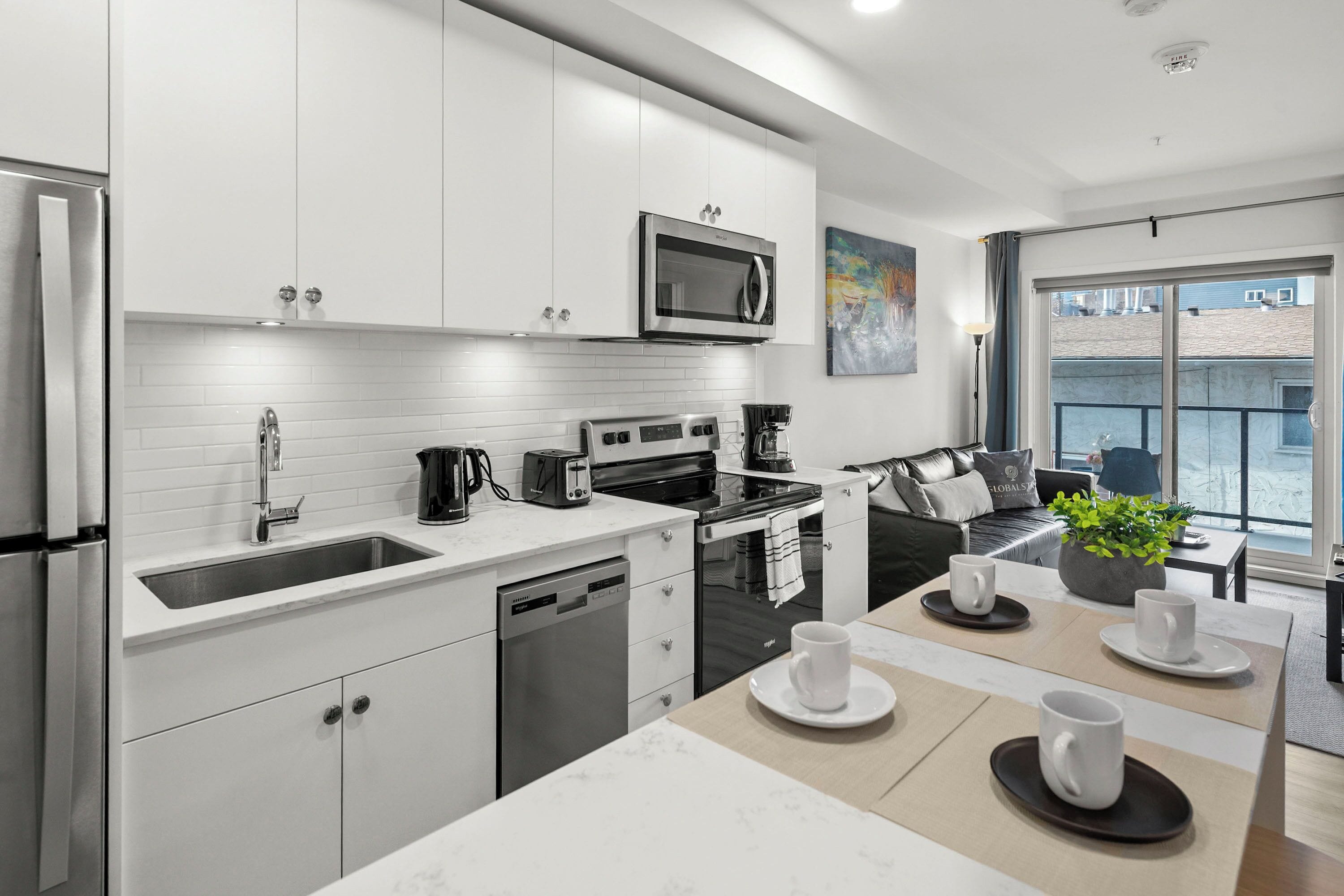 Une cuisine moderne avec des meubles blancs, des appareils en acier inoxydable et un coin repas avec une table dressée pour deux personnes.