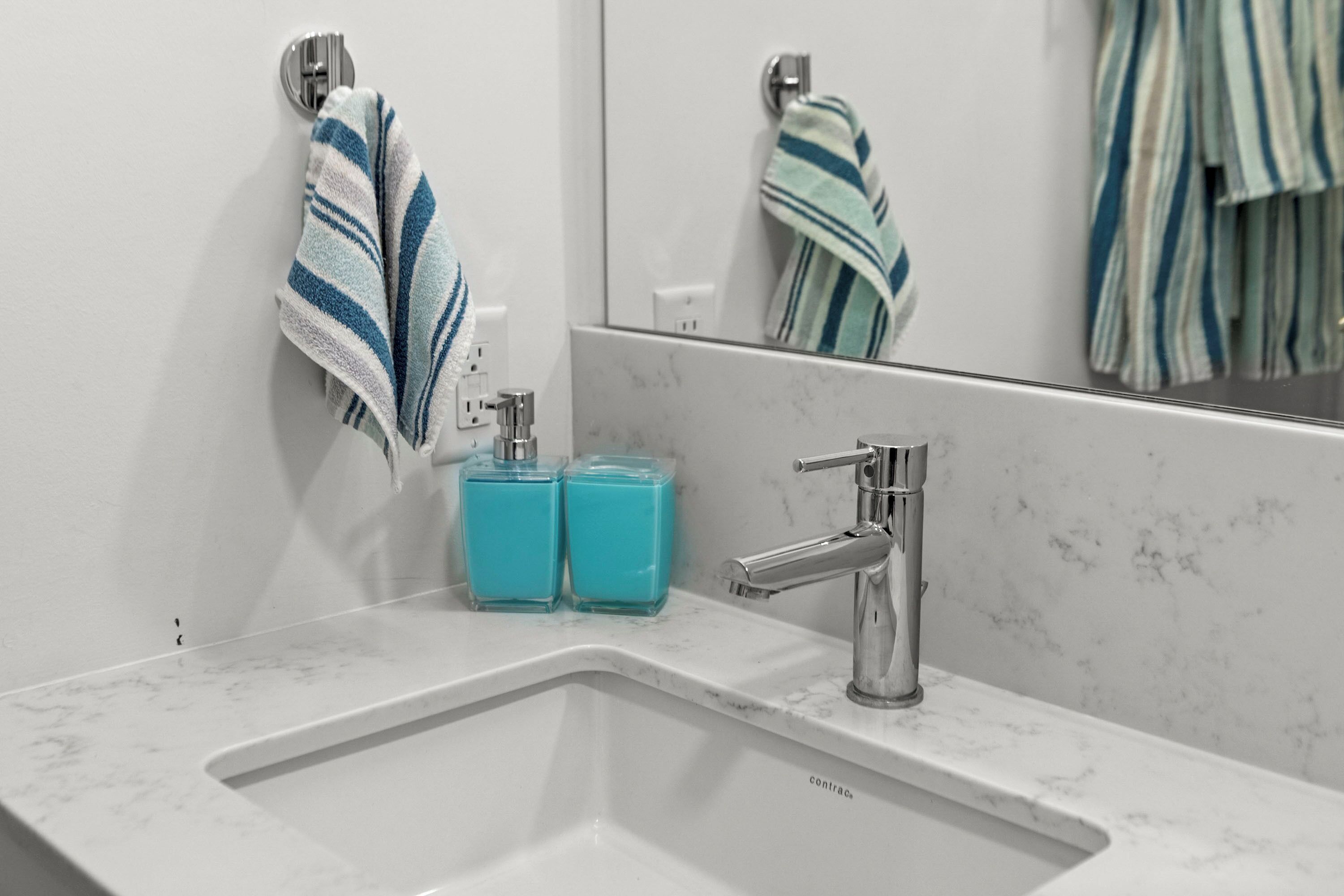 A bathroom with a white sink, two blue soap dispensers, and a striped towel hanging on a hook.